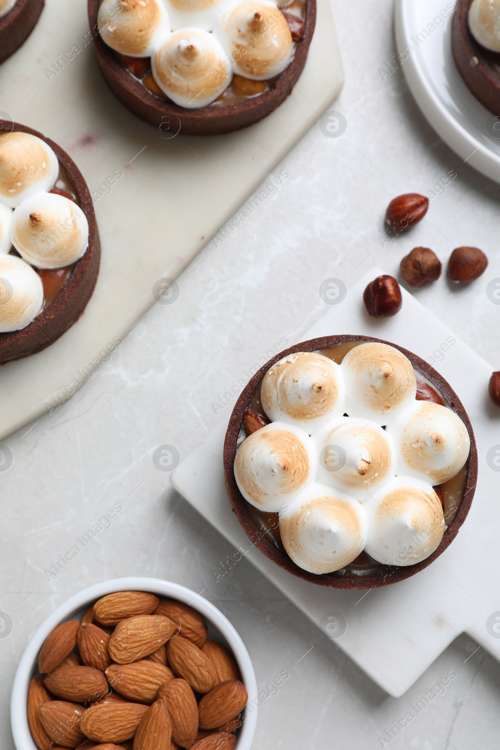Photo of Delicious salted caramel meringue tarts and nuts on light grey marble table, flat lay
