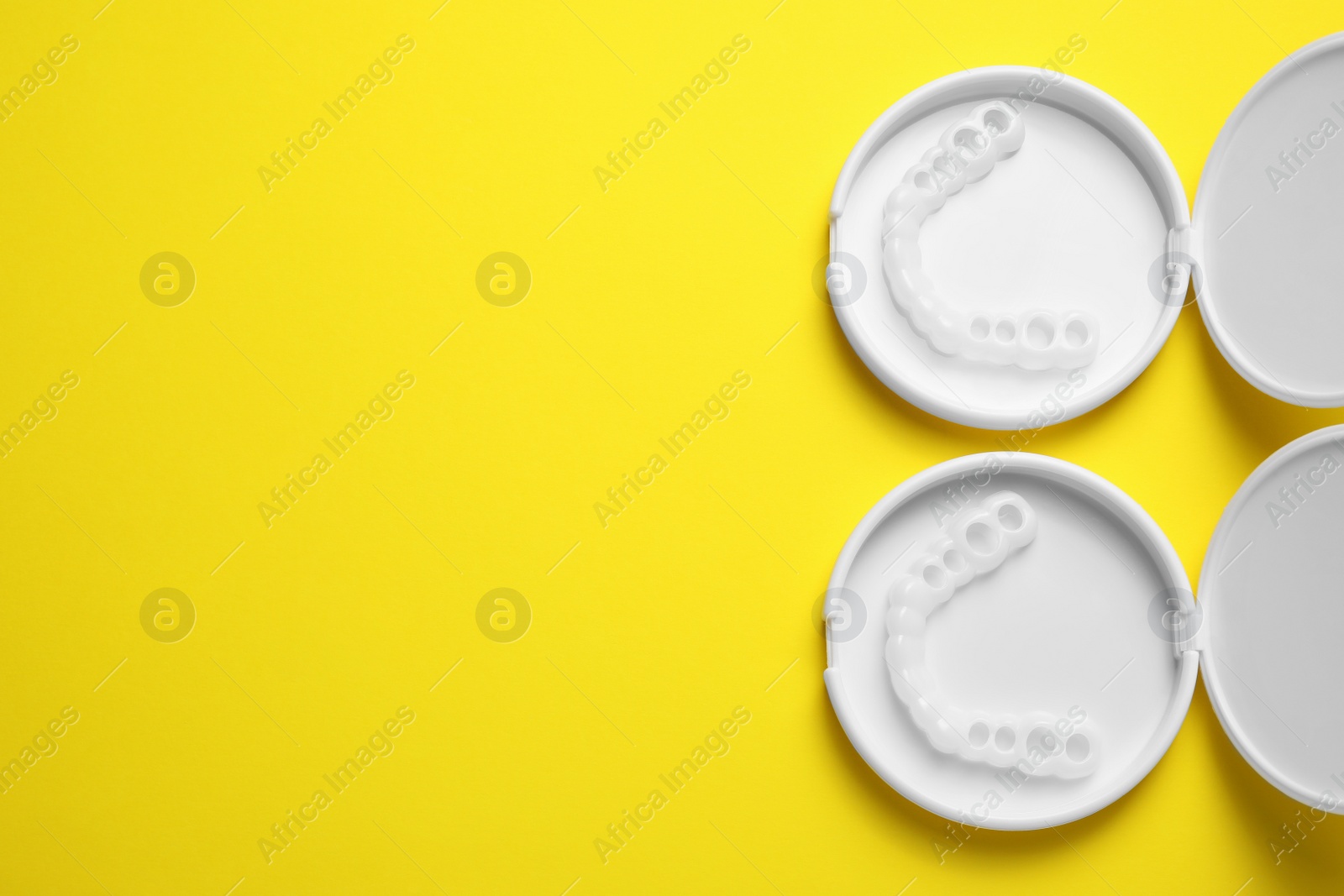 Photo of Dental mouth guards in containers on yellow background, flat lay with space for text. Bite correction