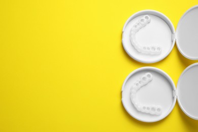 Dental mouth guards in containers on yellow background, flat lay with space for text. Bite correction