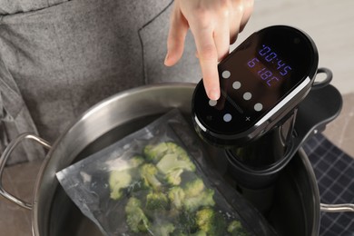 Photo of Woman using thermal immersion circulator in pot with broccoli, closeup. Sous vide cooking