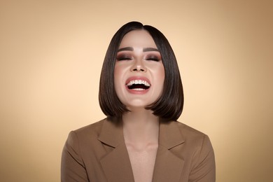 Image of Portrait of stylish young woman with brown hair laughing on beige background