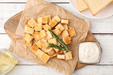 Photo of Delicious crispy croutons with rosemary and sauce on white wooden table, flat lay