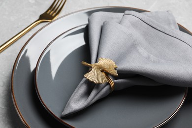 Photo of Plates with gray fabric napkin and decorative ring in table, closeup