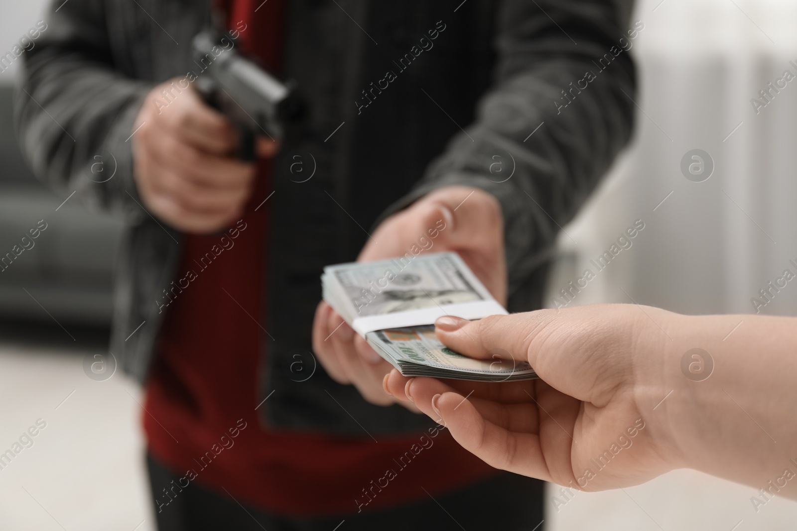 Photo of Woman giving money to criminal with gun indoors, closeup. Armed robbery