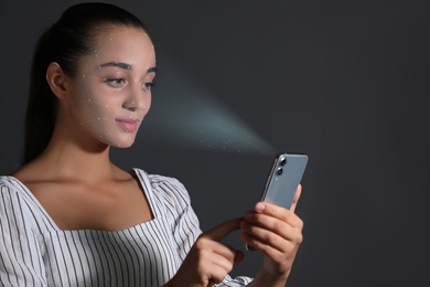 Young woman unlocking smartphone with facial scanner on black background. Biometric verification