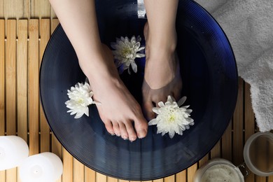 Woman soaking her feet in bowl with water and flowers on floor, top view. Spa treatment