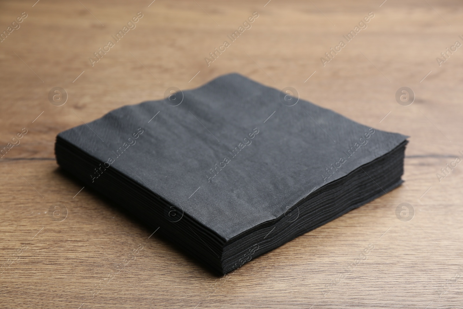 Photo of Stack of black clean paper tissues on wooden table