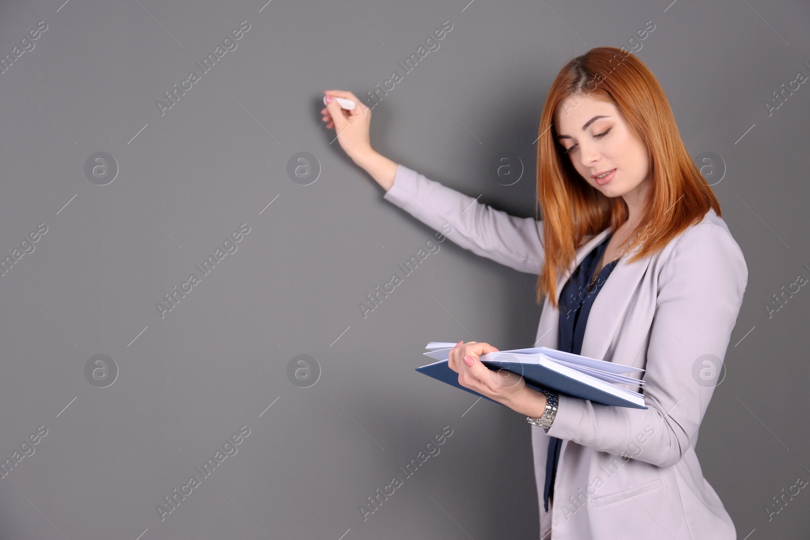 Photo of Beautiful young teacher with chalk and book on grey background