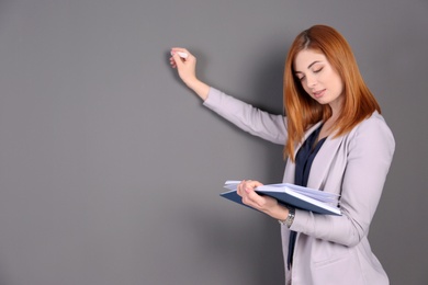 Beautiful young teacher with chalk and book on grey background