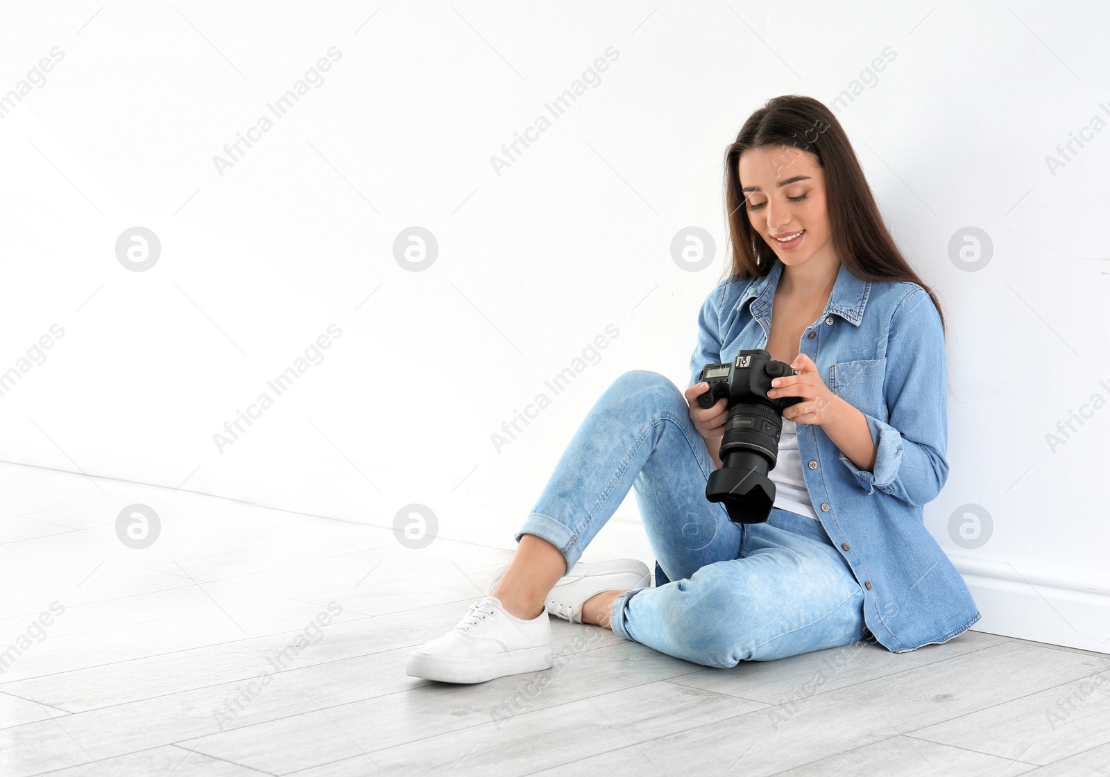 Photo of Female photographer with camera sitting on floor near wall indoors