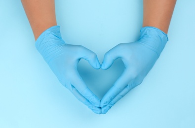 Photo of Person in latex gloves showing heart gesture against light blue background, closeup on hands