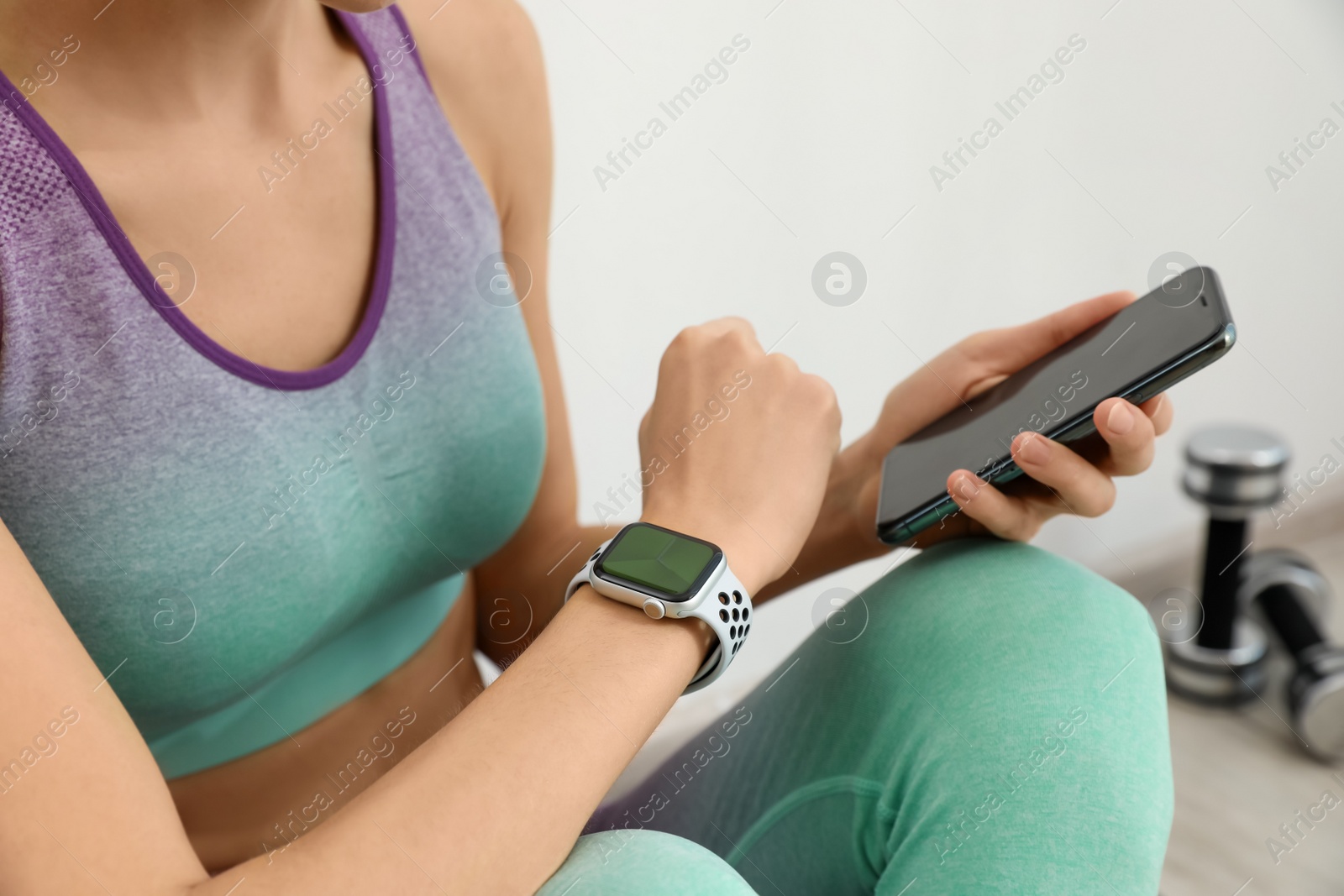 Photo of Young woman with modern smart watch and phone indoors, closeup