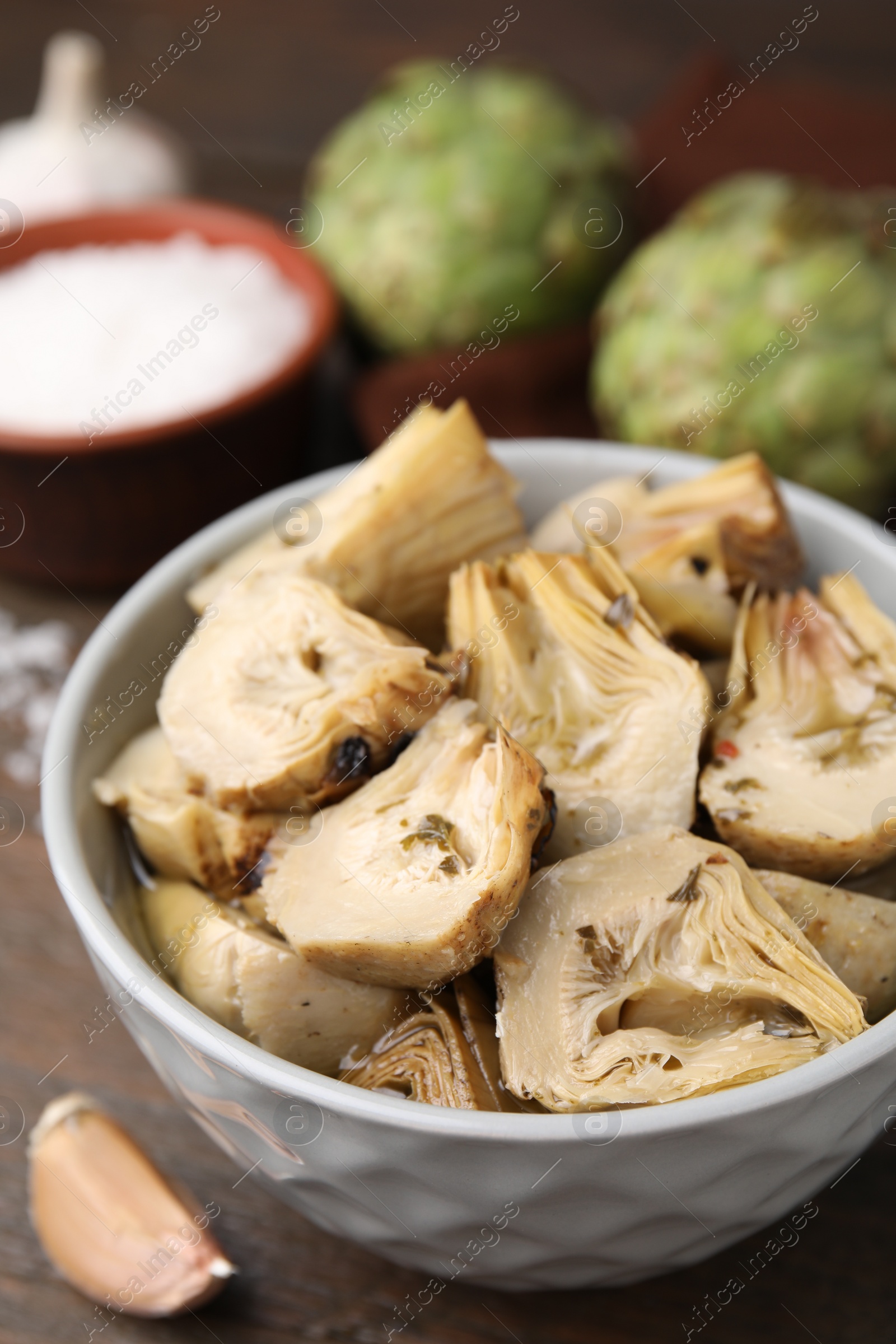 Photo of Bowl of pickled artichokes on wooden table, closeup