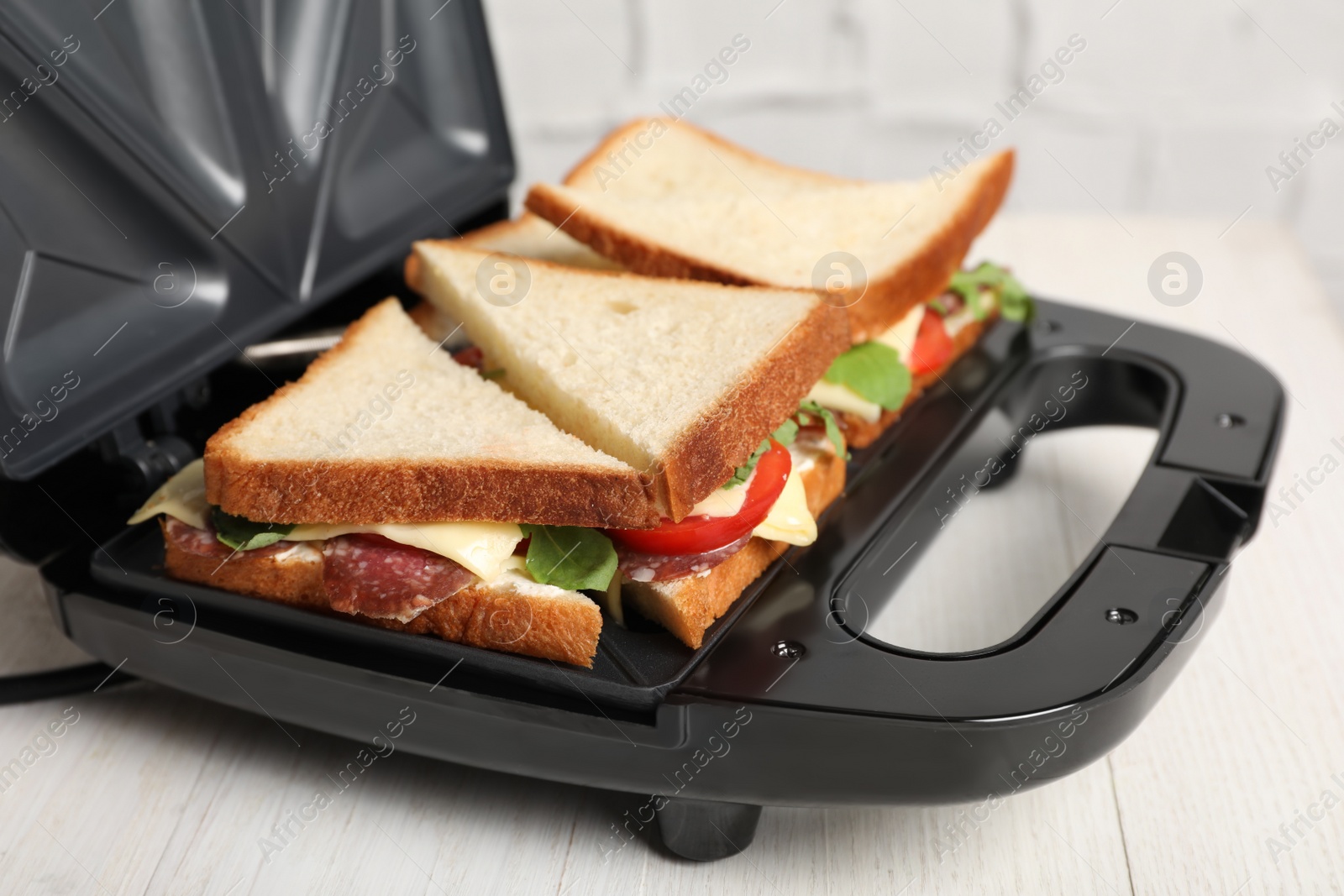 Photo of Modern grill maker with tasty sandwiches on white wooden table, closeup view