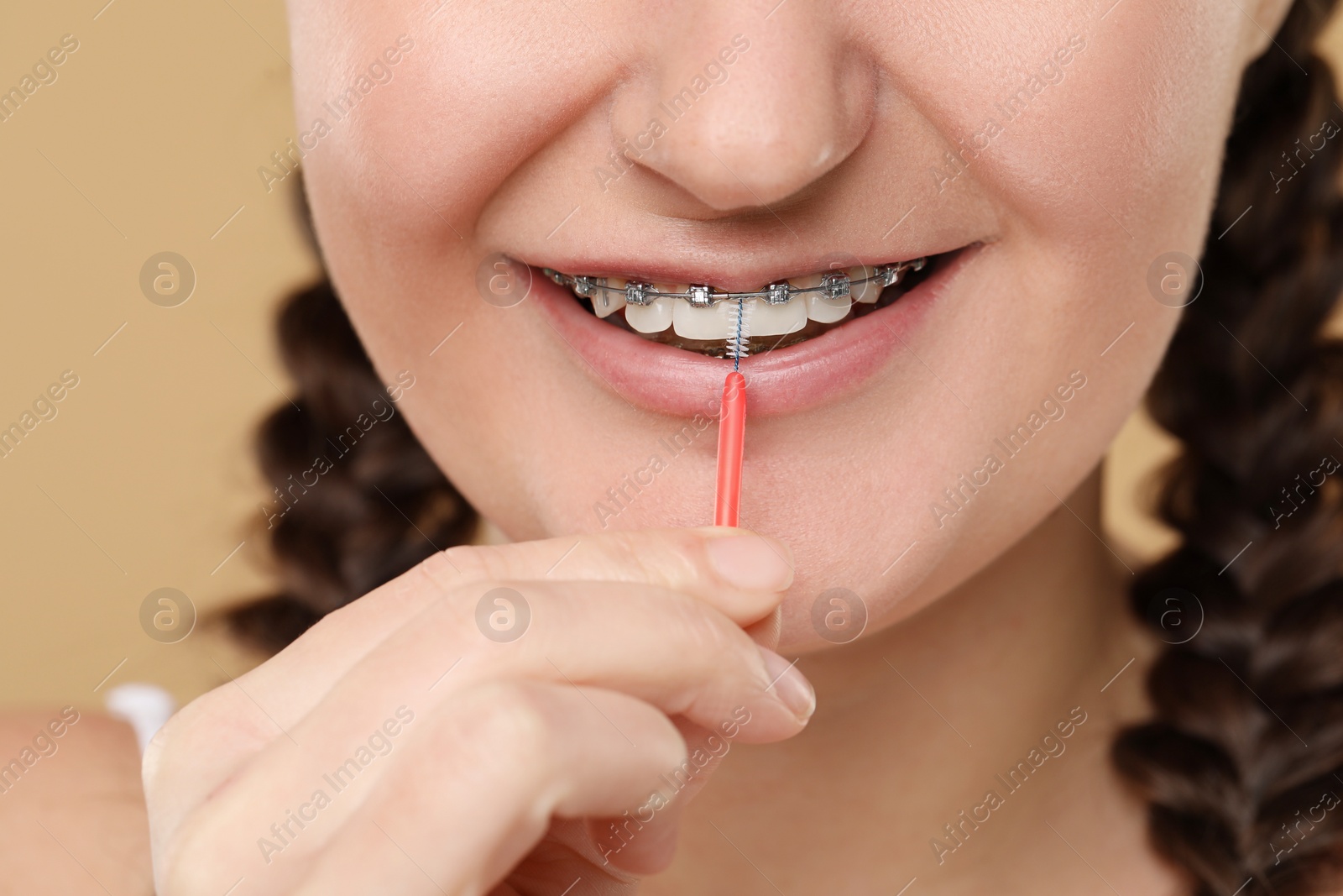 Photo of Woman with dental braces cleaning teeth using interdental brush on brown background, closeup