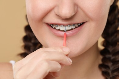 Photo of Woman with dental braces cleaning teeth using interdental brush on brown background, closeup