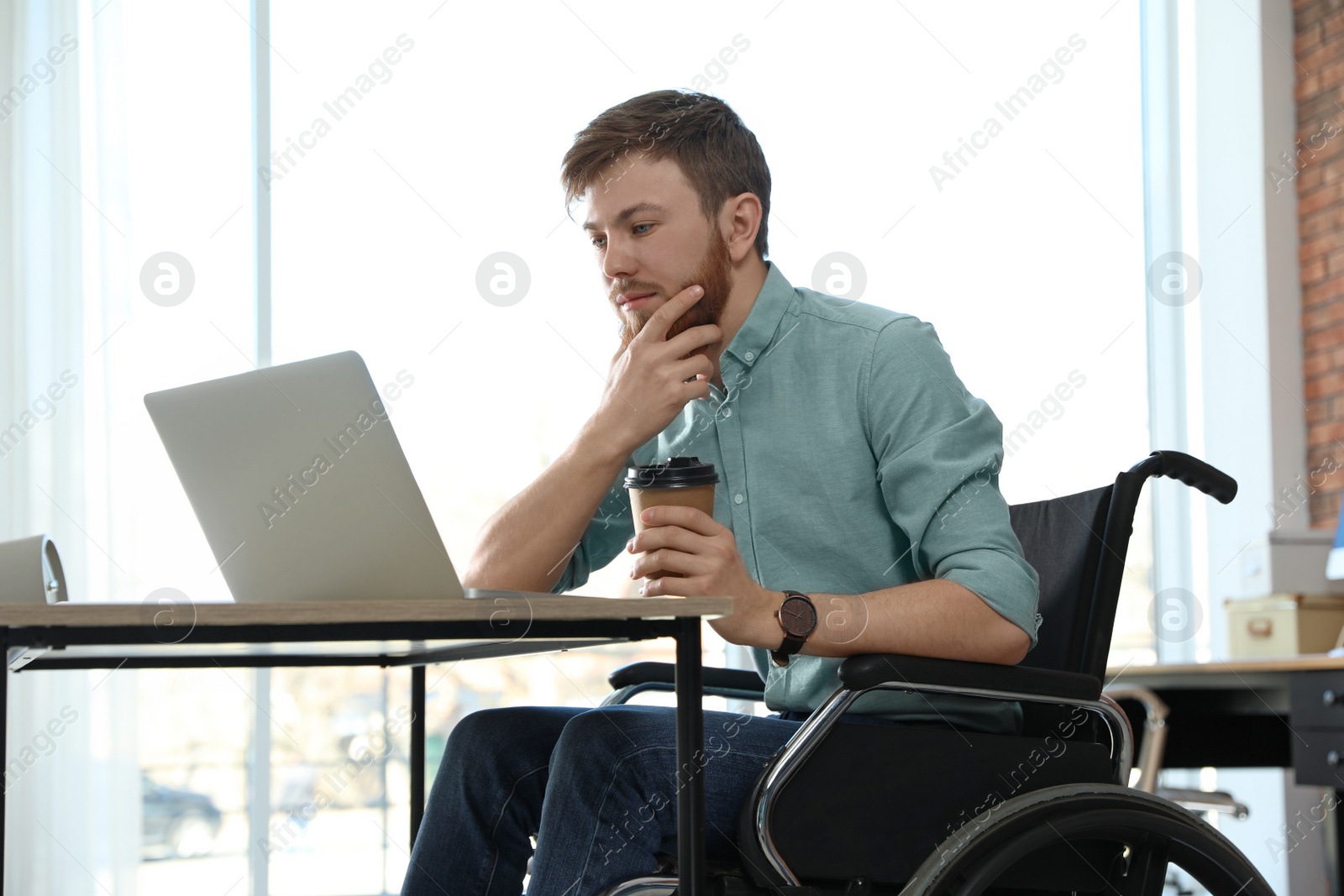 Photo of Young man in wheelchair using laptop at workplace