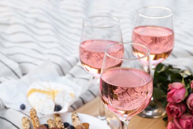 Glasses of delicious rose wine, flowers and food on white picnic blanket, closeup