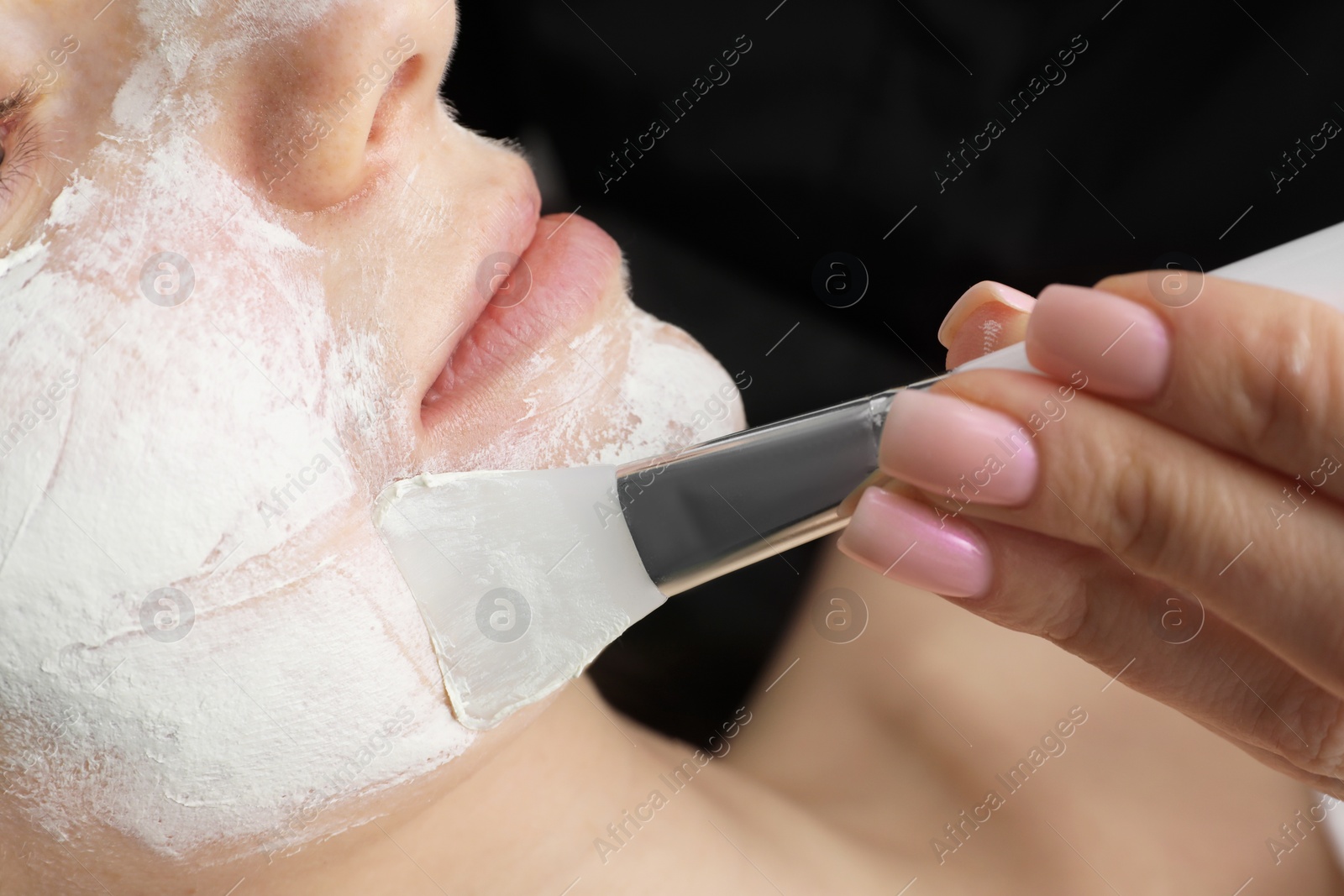 Photo of Cosmetologist applying mask on woman's face, closeup