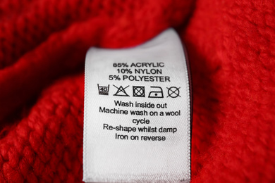 Clothing label with care symbols and material content on red sweater, closeup view