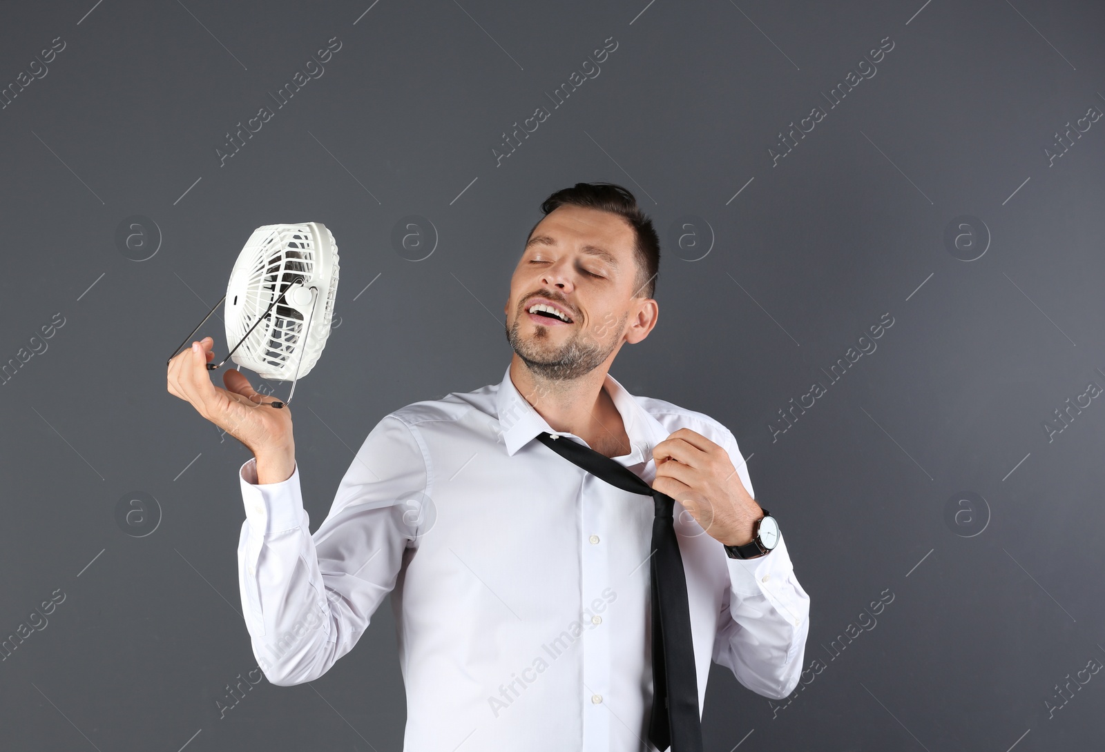 Photo of Man refreshing from heat in front of fan on grey background