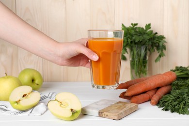 Photo of Woman holding glass of carrot juice at white wooden table, closeup