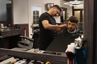 Photo of Professional hairdresser making stylish haircut near mirror in barbershop