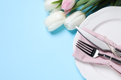Photo of Stylish table setting with cutlery and tulips on light blue background, flat lay. Space for text
