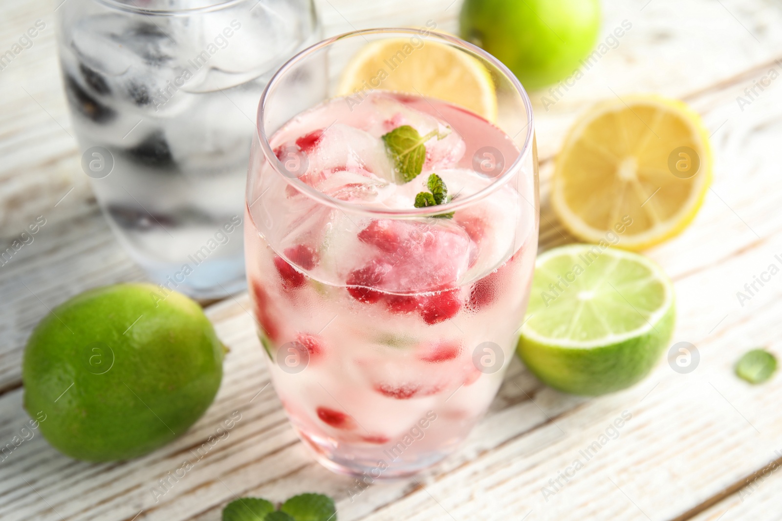 Photo of Glass of drink with pomegranate ice cubes on wooden background