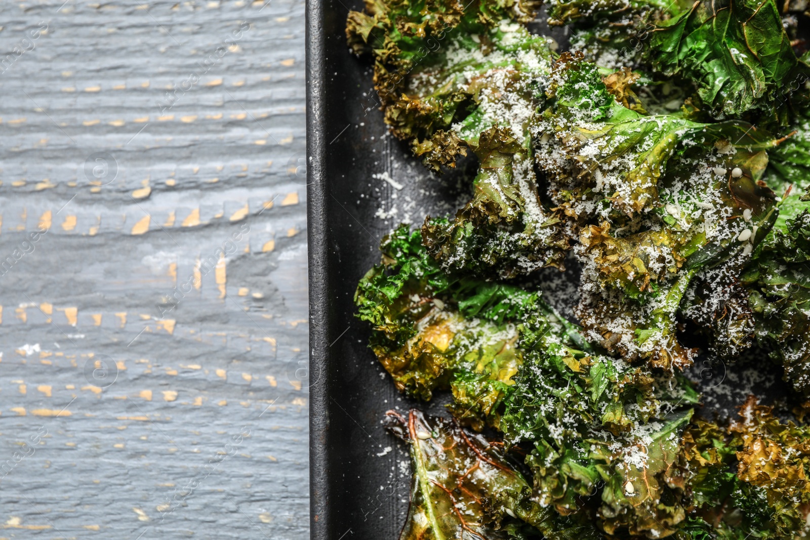 Photo of Tasty baked kale chips on light grey wooden table, top view. Space for text