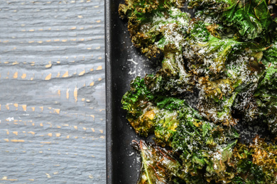 Tasty baked kale chips on light grey wooden table, top view. Space for text