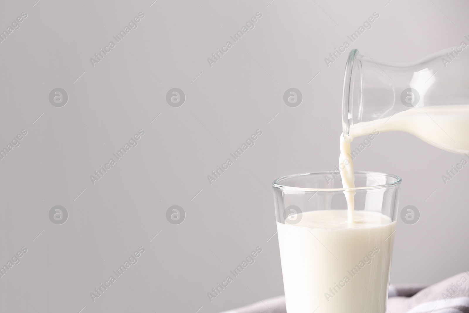 Photo of Pouring milk into glass on grey background. Space for text