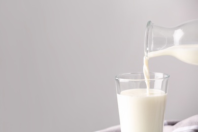 Pouring milk into glass on grey background. Space for text