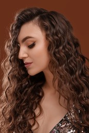 Beautiful young woman with long curly hair on brown background, closeup