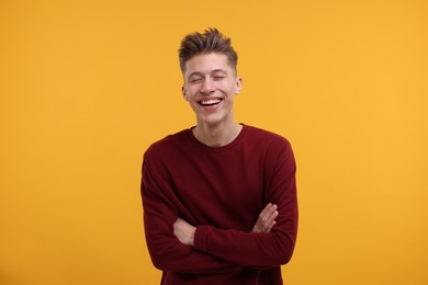 Photo of Portrait of young man with crossed arms laughing on orange background