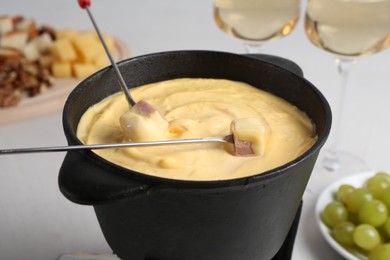 Photo of Dipping ham into fondue pot with tasty melted cheese at white table, closeup