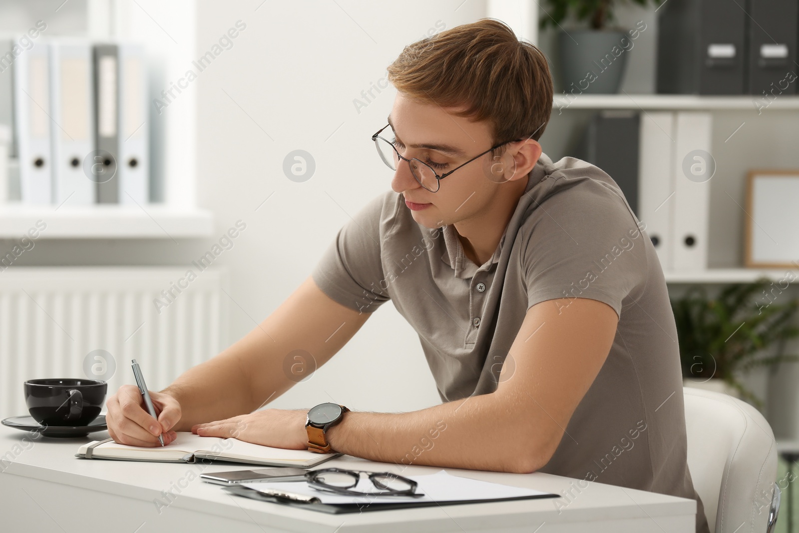 Photo of Young man writing in notebook at table indoors