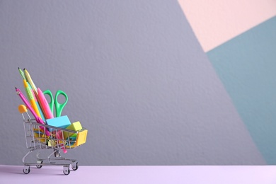 Photo of Small shopping cart with different school stationery on color background. Space for text