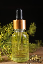 Bottle of essential oil and fresh dill on wooden table, closeup