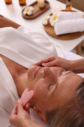 Photo of Woman receiving facial massage with rose quartz gua sha tool in beauty salon, closeup
