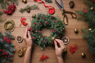 Florist making beautiful Christmas wreath at wooden table, top view