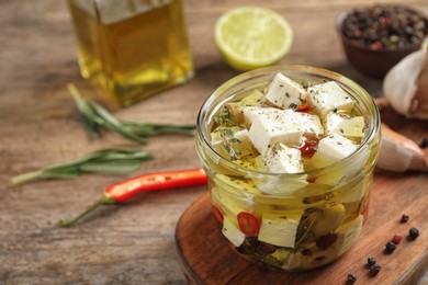 Glass jar of marinated feta cheese on wooden table