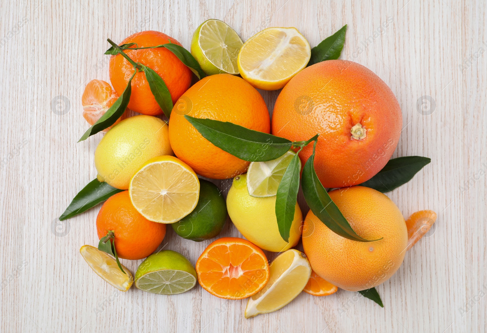 Photo of Different citrus fruits with fresh leaves on white wooden table, flat lay