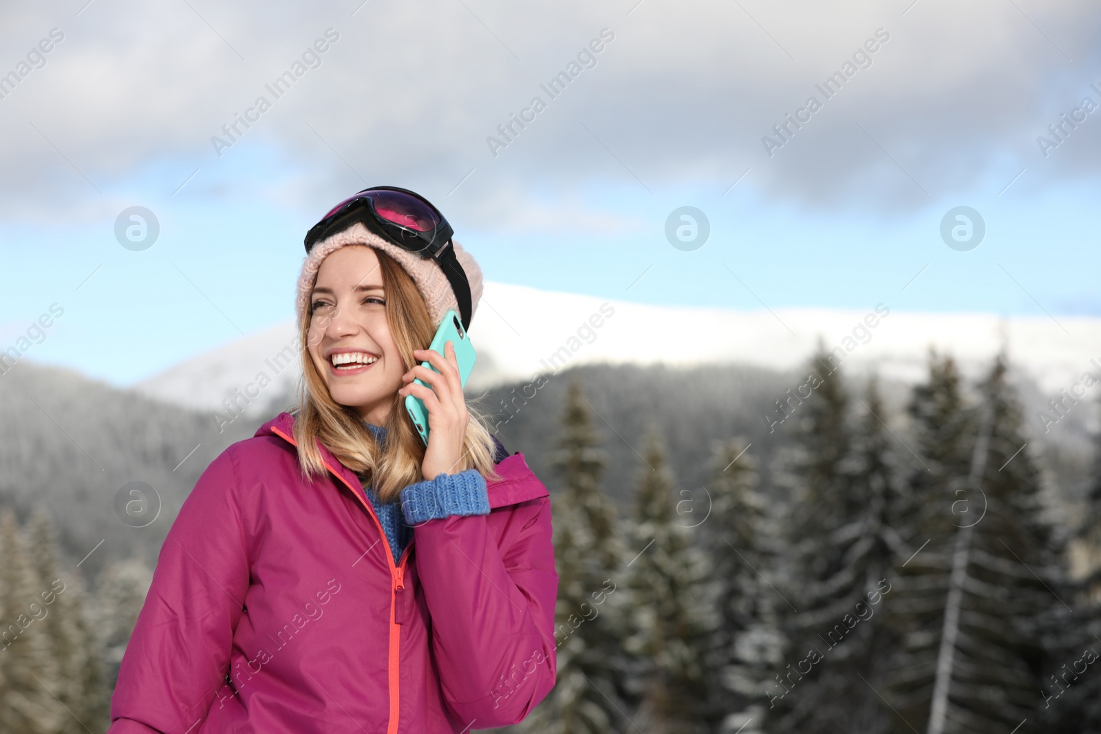 Photo of Young woman with ski goggles talking on phone in mountains during winter vacation. Space for text