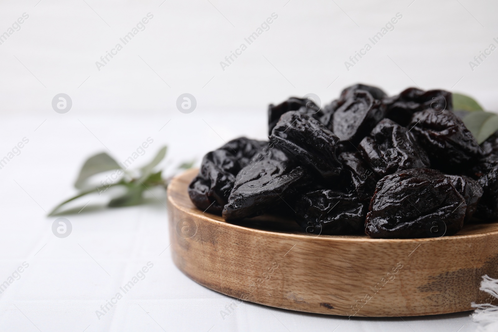 Photo of Sweet dried prunes on white tiled table, closeup. Space for text