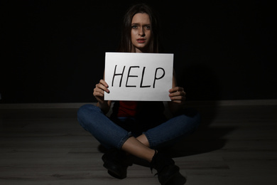 Abused young woman with sign HELP on black background. Domestic violence concept