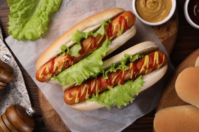 Tasty hot dogs and ingredients on wooden table, flat lay