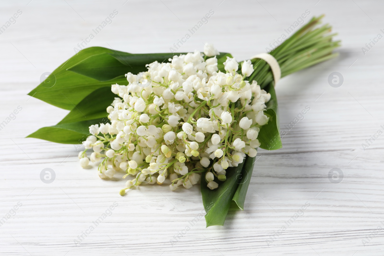 Photo of Beautiful lily of the valley bouquet on white wooden table