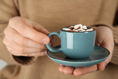 Photo of Woman holding cup of delicious hot chocolate with marshmallows and syrup, closeup