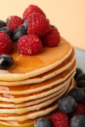 Photo of Stack of tasty pancakes with raspberries, blueberries and honey on pale orange background, closeup